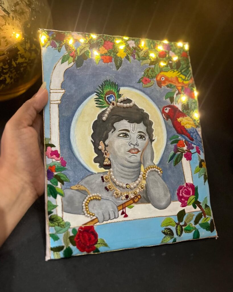 Embroidery artwork of young Lord Krishna with jewelry and parrots, surrounded by flowers and foliage