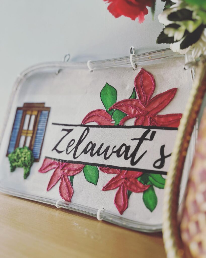Hand-embroidered name plate with “Zelawat’s” stitched in decorative thread on fabric